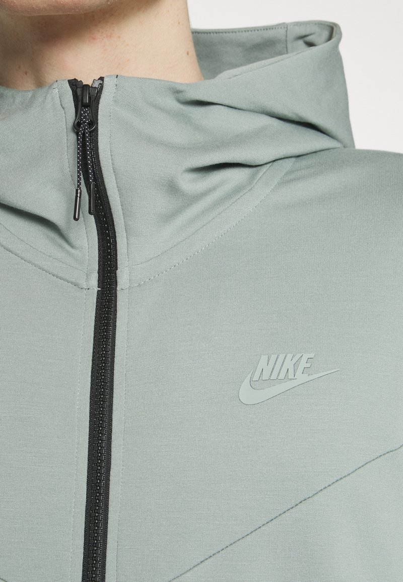 Haut de hoodie Nike vert clair avec fermeture éclair à l'avant, tissu texturé et logo subtil sur la poitrine. Comprend une capuche et des coutures plates.