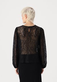 Mustmustest lace blouse pikade pikkade puffvarrukatega, millel on võtmeaugu tagune detail ja sujuv kangast paneel all. Peenelt tikitud lillemuster.