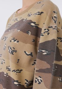 Μπεζ και καφέ μακρυμάνικο τοπ με υφή πλεκτού τύπου βάφλ και σχέδια καμουφλάζ και αφαίρεσης σε σκούρα και ανοιχτά χρώματα.