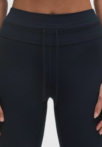 Mørkeblå højtaljede leggings med snorelukning og glat, struktureret stof. Ingen synlige lommer eller mønstre. Nævn giver synlig sømsyn.