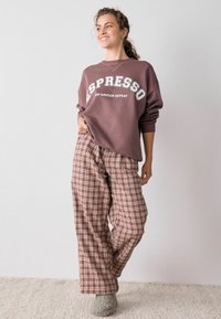 Brun sweatshirt med teksten "ESPRESSO", parret med ternede bukser i brun og creme. Blød tekstur og afslappet pasform. Hygge sokker fuldender looket.