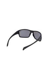 Gafas de sol negras con lentes grises, diseño deportivo, montura curva y brazos delgados. Cuentan con un leve recubrimiento antirreflectante.