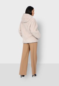 Jasno beżowy puszysty hoodie o luźnym kroju i kapturem, sparowany z szerokimi spodniami w odcieniu tan, tworząc miękki, teksturowany wygląd.