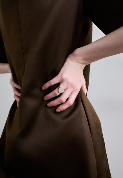 Pruun kangaskleit, millel on sile tekstuur, lühikesed varrukad ja figuuri rõhutav vöökoht, mida täiendab kuldne ja valge südamekujuline sõrmus.