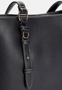 Czarna skórzana torebka o gładkiej fakturze, z kontrastującym białym szwem i złotym pierścieniem na odpinanym pasku.