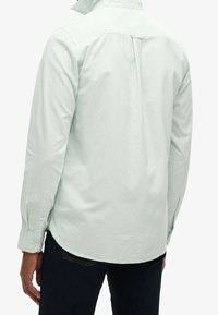 Lichtmintgroen shirt met lange mouwen, een button-down kraag, achterplooidetail en met knopen gesloten manchetten, gecombineerd met donkere spijkerbroek.