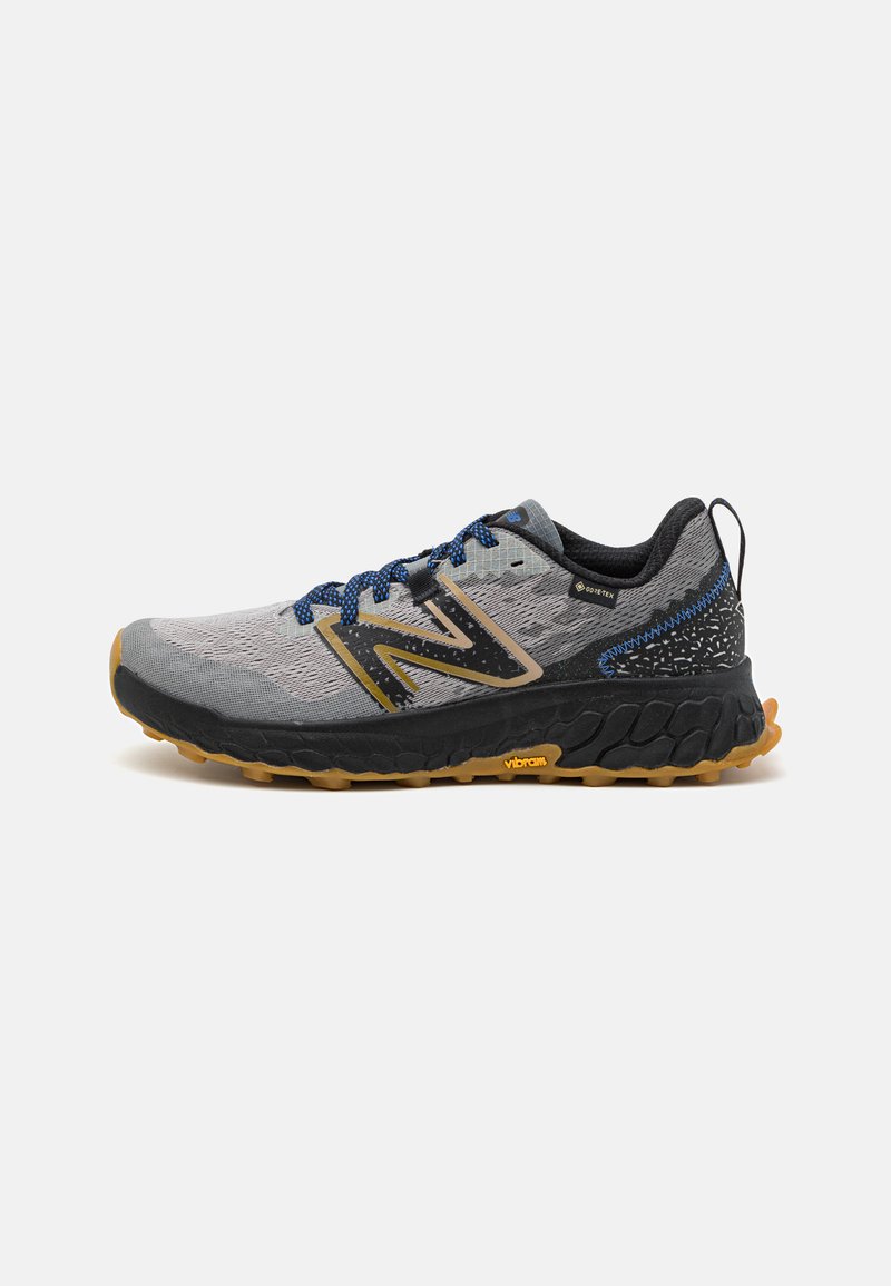 Grå og svart løpesko med teksturert overdel, blå lisser og Vibram såle. Har en Gore-Tex vanntett fôr og dristig logodesign.