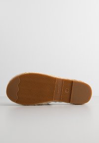 Light brown rubber shoe sole with wave pattern and embossed logo. Textured edge with a soft, light-colored upper material visible.