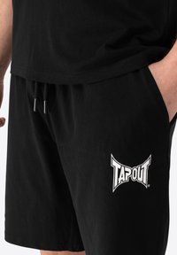 Fekete pamut rövidnadrág rugalmas derékkal, bal oldalon fehér "TAPOUT" logóval. Texturált anyag és zsinóros részlet.