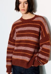 Oversized trui in bruin, roze en oranje strepen; gemaakt van zacht, pluizig materiaal met brede mouwen en een ronde hals.