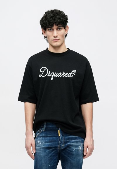 Black oversized t-shirt with white "Dsquared²" logo, round neck, and short sleeves, paired with distressed blue jeans.
