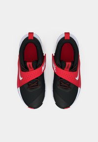 Nike sporta apavi ar melnu augšdaļu, sarkaniem akcentiem un baltu apdari. Iekļauj teksturētu siksnu un auklas drošai piestiprināšanai.