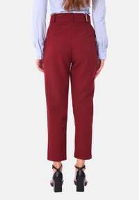 Pantaloni tailored bordeaux a vita alta, con passanti per cintura, texture liscia e tasche oblique. Indossati con sandali neri con tacco a blocco.