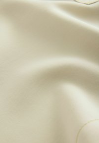 Tejido texturizado beige con un sutil patrón de estrías y superficie lisa, adecuado para diversas aplicaciones. Material suave y ligero.