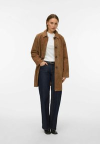 Pruun seemisnahast mantel kraega, esikinnis ja pikkade varrukatega. Ühitatud tumeliste laiade pükstega. Alla lihtne valge särk.