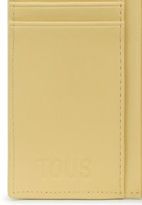 Tarjetero de cuero amarillo que cuenta con múltiples ranuras para tarjetas y el logo "TOUS" en relieve. Textura suave con fina costura en los bordes.