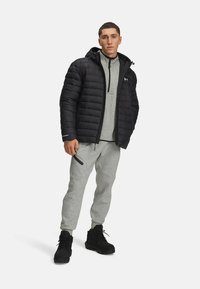 Sort pufjakke med hætte, grå fleece zip-up top, grå sweatpants og sorte støvler. Har et slankt, moderne design og tekstureret stof.