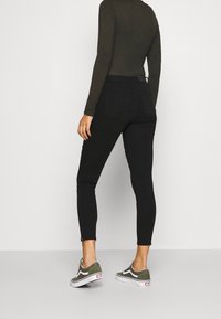 Jeans negros ajustados de cintura alta, con dos bolsillos traseros y un diseño desgastado. Combinados con zapatillas de lona verde oliva.