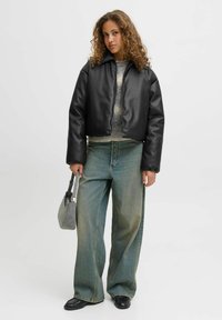 Czarna krótka kurtka z gładkiego materiału, z wysokim kołnierzem i zapięciem na zamek, w połączeniu z jasnoniebieskimi dżinsami o szerokich nogawkach i szarym torebką.