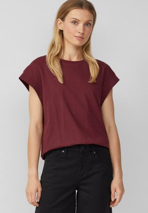 Burgunderfarbenes T-Shirt mit kurzen Ärmeln, runden Halsausschnitt und lockerer Passform. Der Stoff wirkt weich mit einer glatten Textur, kombiniert mit schwarzen Jeans.