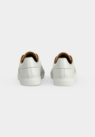 Paire de baskets basses blanches avec doublure intérieure marron vue de dos sur un fond gris clair uni.