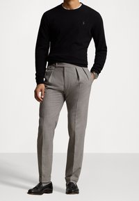 Pull noir en maille, pantalon plissé gris en tissu texturé, et chaussures en cuir noir. Design simple avec une coupe ajustée et des détails soignés.