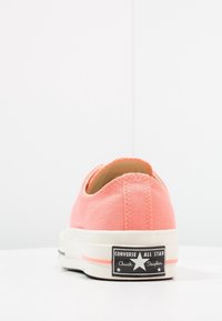 Korallowe płócienne trampki z niskim krojem, biała gumowa podeszwa oraz czarną metką z logo "Converse All Star Chuck Taylor".