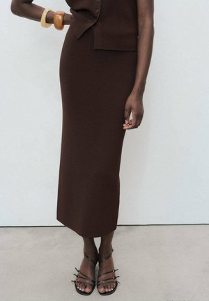 Brown ribbed knit dress with a fitted silhouette, paired with black strappy sandals featuring decorative hardware. Smooth texture throughout.