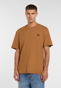 Brun kortærmet t-shirt lavet af bomuld, med en rund hals og et logo trykt i sort på venstre brystområde.