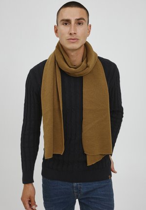 Brown knitted scarf draped around the neck, paired with a navy cable-knit sweater. The scarf displays a soft texture and regular shape.