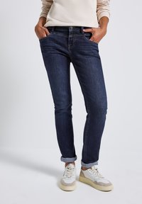 Mörkblå denimjeans med slim fit, i klassisk femfickdesign och uppvikta benslut, i kombination med vita och beige sneakers.