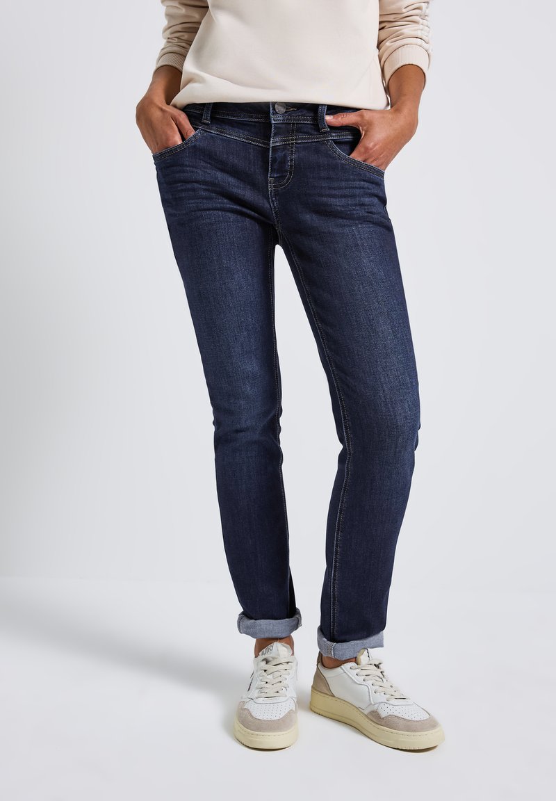 Mörkblå denimjeans med slim fit, i klassisk femfickdesign och uppvikta benslut, i kombination med vita och beige sneakers.
