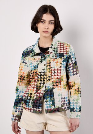 Jacke mit mehrfarbigem Hahnentrittmuster aus strukturiertem Stoff, mit Kragen, Knopfverschluss und Klapptaschen, kombiniert mit beigen Shorts.