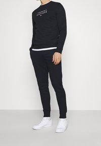 Czarna bluza z kapturem z białym logo "TOMMY HILFIGER", w parze z czarnymi tapered spodniami i białymi sneakersami. Luźny, wygodny fason.