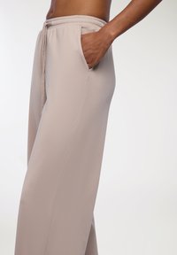 Jasnobeżowe spodnie o szerokich nogawkach, wykonane z gładkiej tkaniny. Posiadają elastyczny pas i boczne kieszenie. Dopasowany krój z luźnym fasonem.