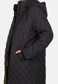 Prošívaná černá péřová bunda s kapucí, s předním zipem, kapsami a kontrastním žlutým podšíváním. Měkká, syntetická tkanina s texturovaným povrchem.