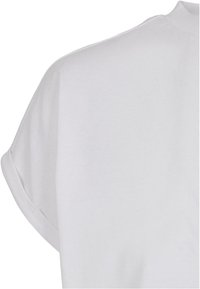 Chemise blanche à manches courtes montrant la zone de l'épaule arrière avec détail de manche retroussée et texture de tissu lisse.