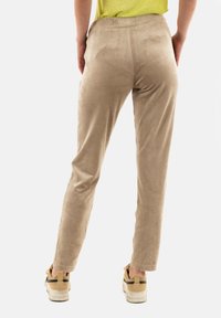 Pantalones de ante beige con ajuste slim, que presentan una textura suave y una cinturilla regular. Llevados con zapatillas de color claro.