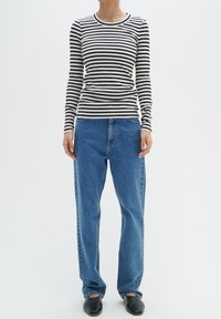 Haut à manches longues rayé blanc et bleu marine, associé à un jean droit bleu clair, port é avec des chaussures noires sans lacets.