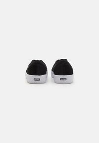Tenisi negri din pânză cu talpă din cauciuc alb, având un design low-top și un detaliu simplu al logo-ului pe spate. Fără modele sau accente vizibile.