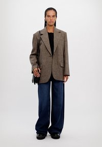 Brown herringbone blazer, black top, loose dark blue jeans, and black chunky shoes, with a small black fringe bag.