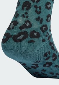 Türkise Socken mit Leopardenmuster, die eine strukturierte Strickart aufweisen, mit großen schwarzen und grauen Flecken, einer gebogenen Ferse und einem gerippten Bündchen für zusätzlichen Komfort.