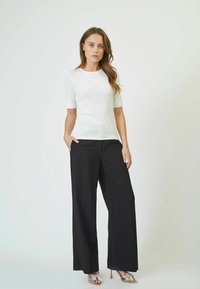 White short-sleeve top paired with wide-leg black trousers and silver bow-accents high-heeled sandals, featuring a smooth texture.