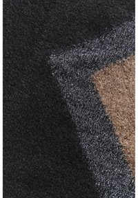 Gros plan sur des couches de tissu texturé en noir, gris foncé avec des fils métalliques, et des fibres de laine brunes.