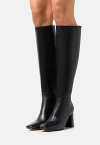 Black leather knee-high boots with a smooth finish, square toes, and block heels, featuring a side zip closure for easy wear.