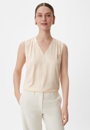 Mouwloze crèmekleurige blouse met een V-hals, voorzien van gathered schouders en een gladde textuur. Gecombineerd met lichte broek.