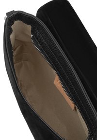 Bolso de cuero negro con cierre de cremallera, con un interior suave y una etiqueta en color marrón. El exterior tiene una superficie texturizada y el diseño es minimalista.