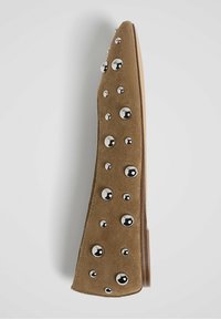 Chaussure plate pointue en daim marron ornée de multiples clous métalliques ronds brillants de différentes tailles sur le dessus.