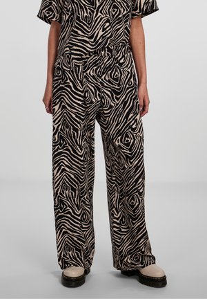 Person iført løse sorte og beige bukser med zebrastriber og matchende top, kombineret med beige sko med tykke sorte såler.