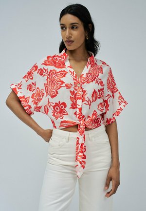 Camisa corta de manga corta con estampado floral rojo y lazo en la parte delantera, hecha de tela ligera, combinada con pantalones blancos de cintura alta.